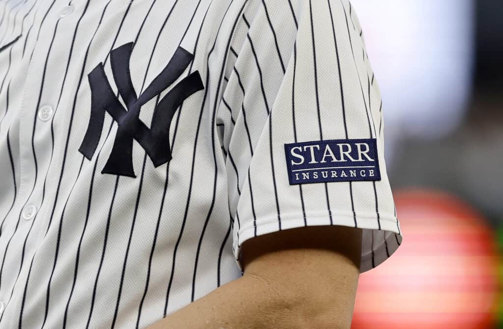 NEW YORK, NEW YORK - JULY 21: A sponsor logo is seen on the sleeve of the uniform of first base coach Travis Chapman #75 of the New York Yankees during a game against the Kansas City Royals at Yankee Stadium on July 21, 2023 in Bronx borough of New York City.